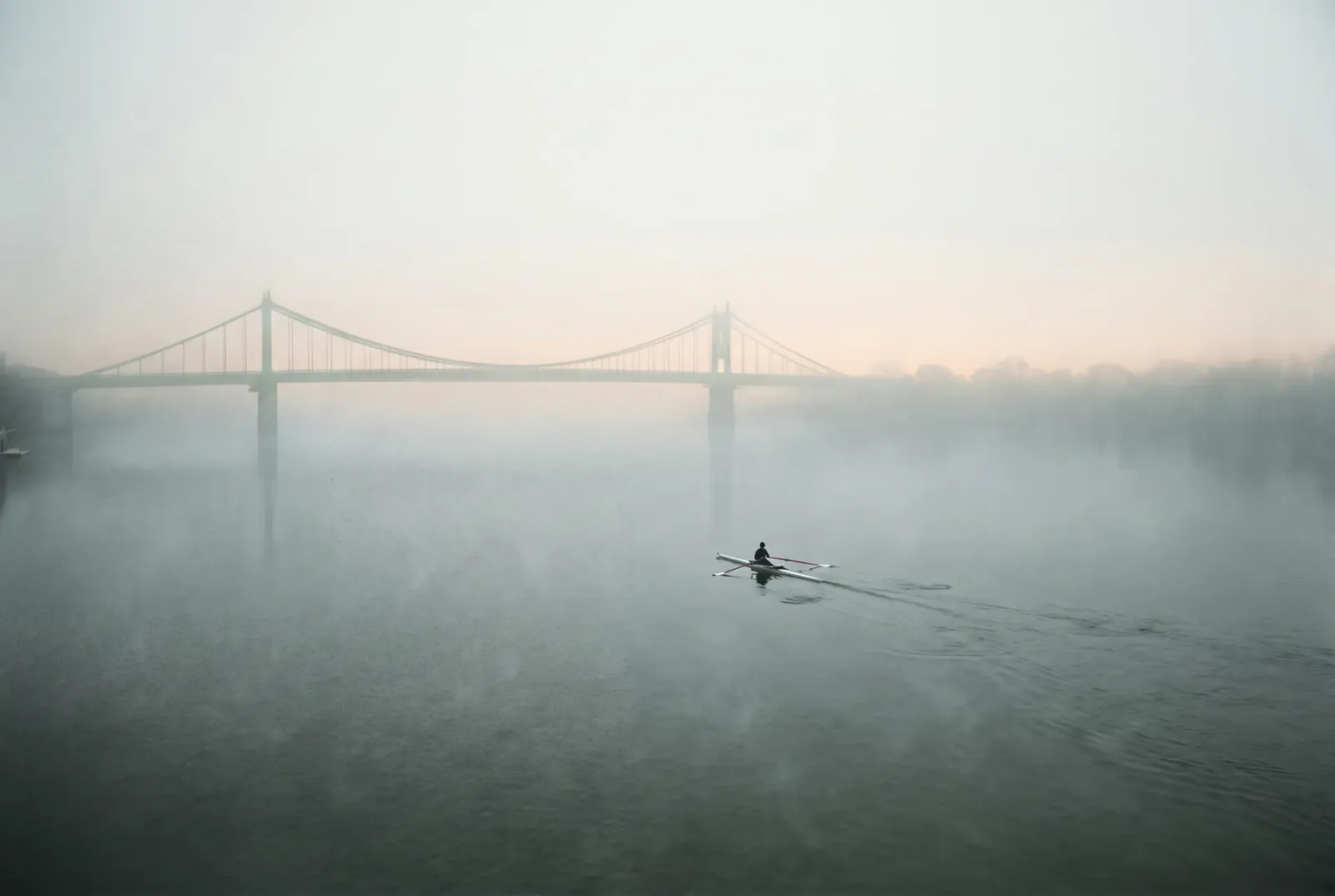 A single rower crossing still water at dawn