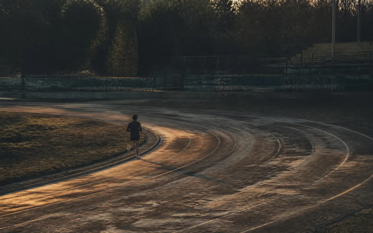 Lone runner rounding the bend of an outdoor track in low evening light