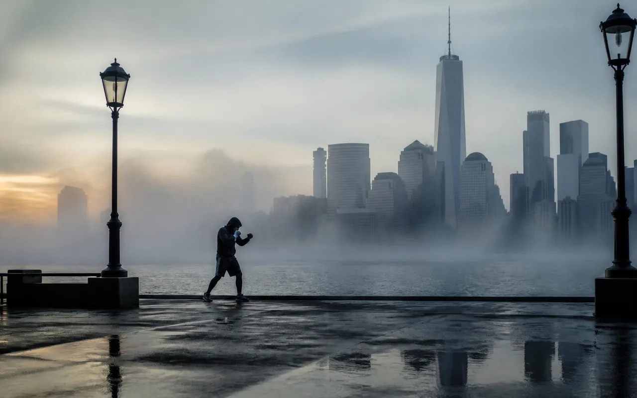 Lone figure shadow boxing on a city waterfront in early morning haze