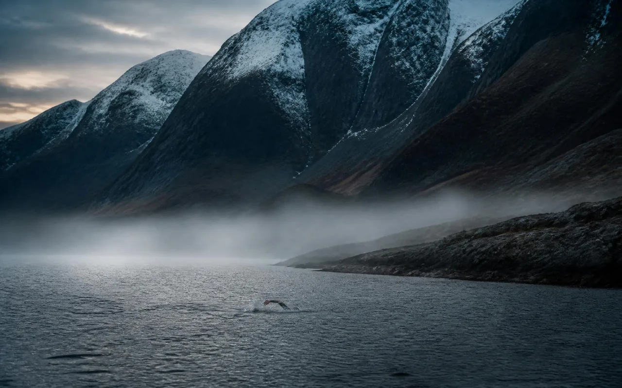 Lone swimmer cutting through dark open water at dawn