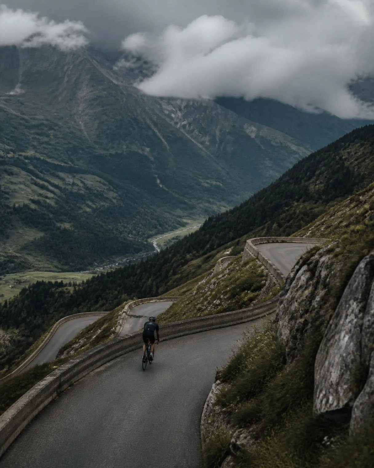 Lone cyclist climbing a switchback road high above a green valley